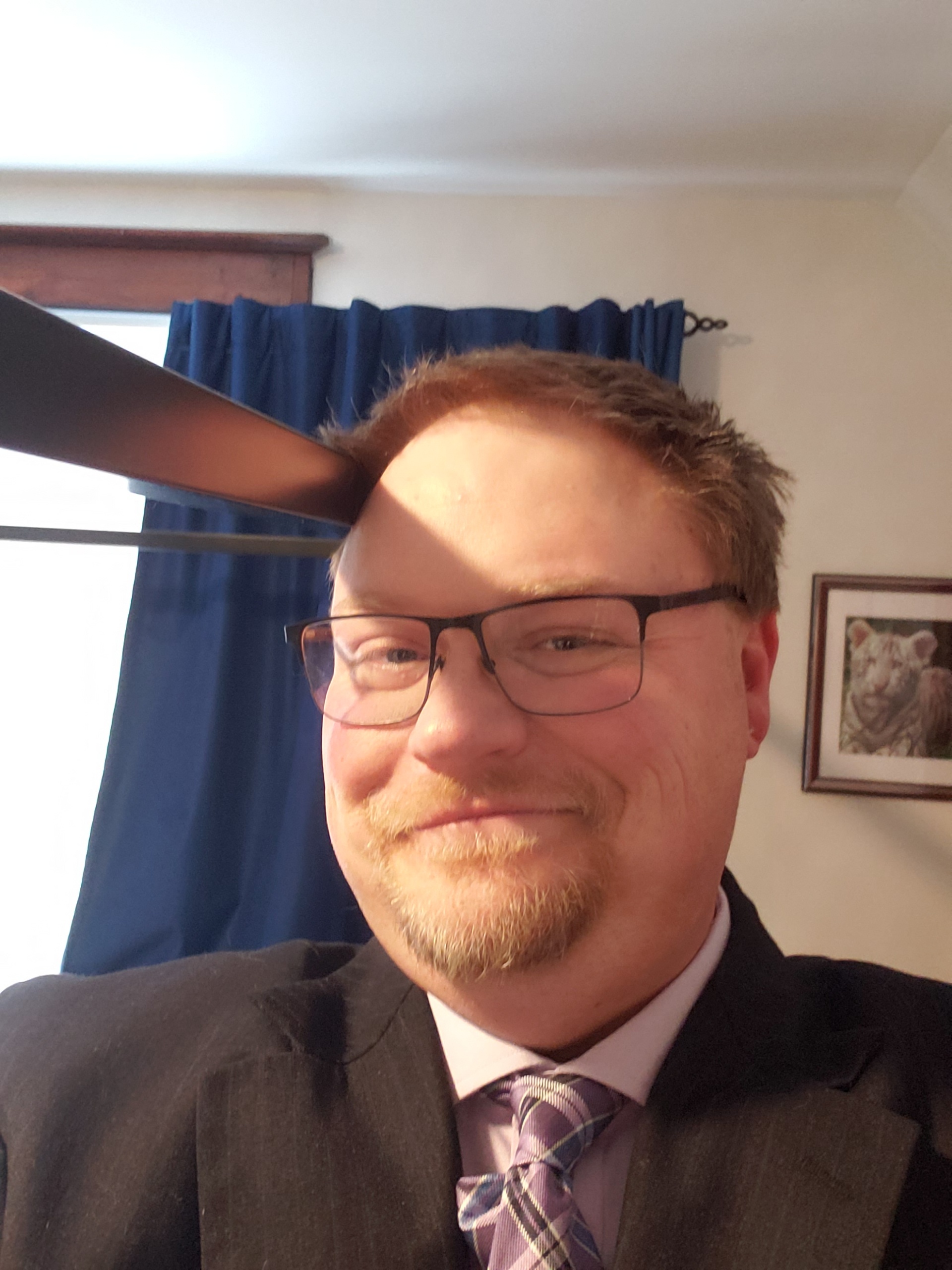 Photo of Andrew Malinski in as suit, smiling and wearing glasses